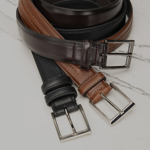 The image features three belt styles lying flat on a black leather surface. Shop the Men’s Accessories category now. 