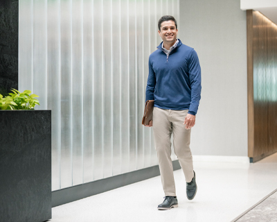 Image features a man in business casual attire walking in a bright office.