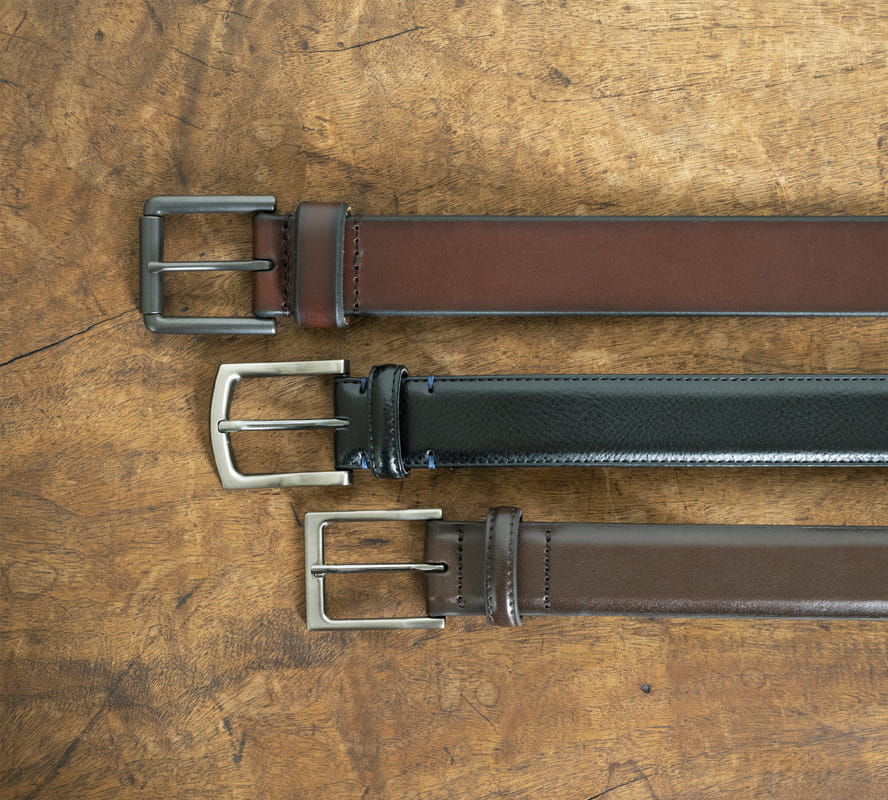 Shop Florsheim belts featuring a variety of styles on a wood surface.