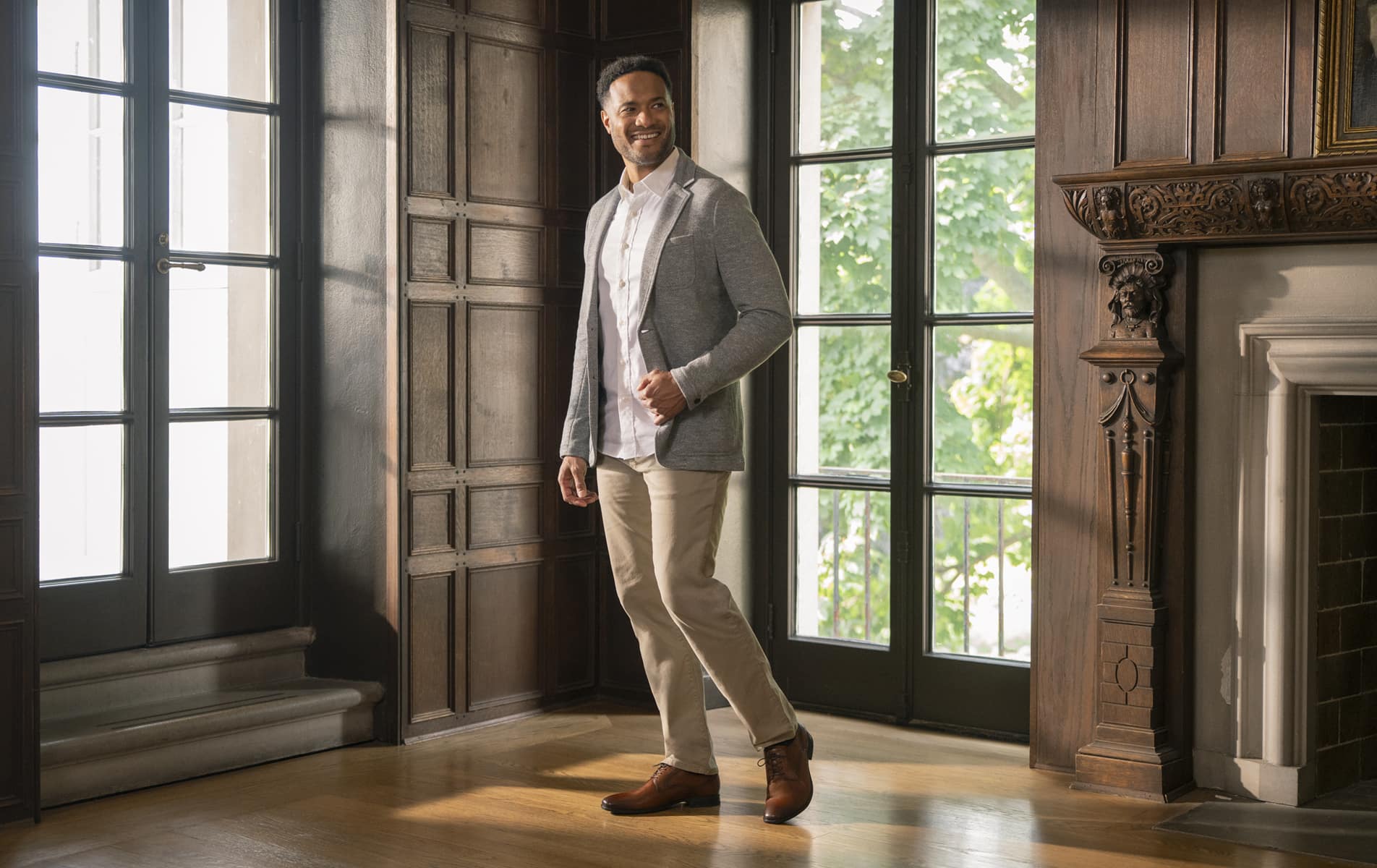 Shop Florsheim dress styles featuring a man standing next to a grand fireplace and windows.