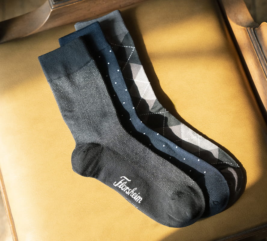 Shop Florsheim accessories featuring a variety of socks on a tan leather background.