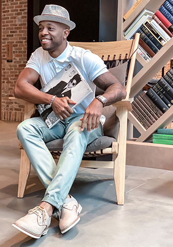 Image of social media influencer Kenny Daniels wearing the Highland Canvas Plain Toe Oxford in Sand while sitting in a chair inside.