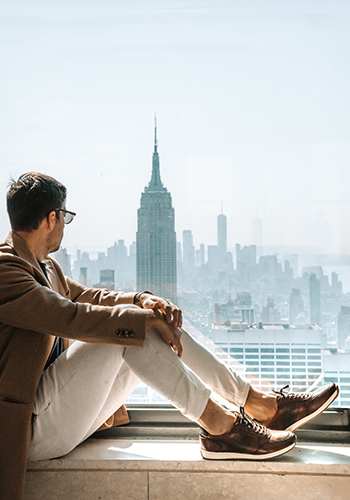 Image of social media influencer Uros Polajzer sitting on a ledge in New York while wearing the Fusion Sport Lace Up in Cognac.