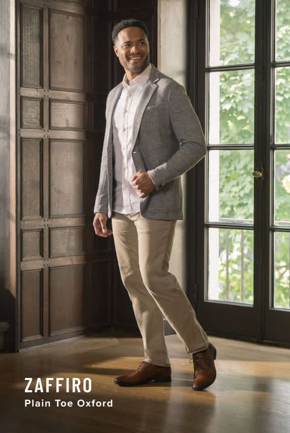 Men's Dress Shoes category. Image features the Zaffiro Plain Toe Oxford in cognac on model in front of large windows.