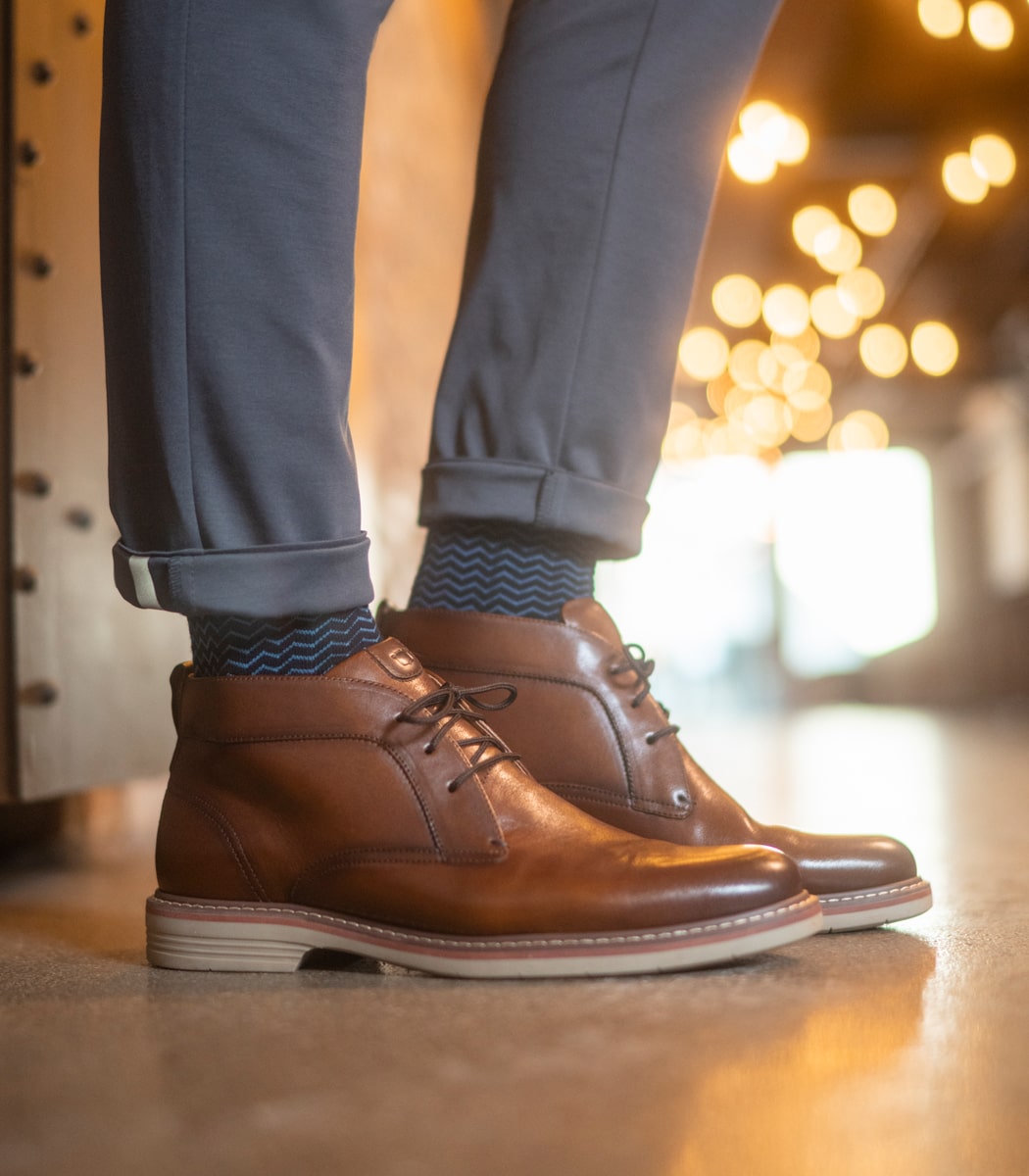 The featured image is a model wearing the Norwalk Plain Toe Chukka Boot in Cognac Tumbled. 
